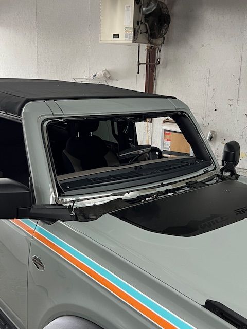 Gray Ford Bronco with windshield removed, parked indoors; side mirror visible.