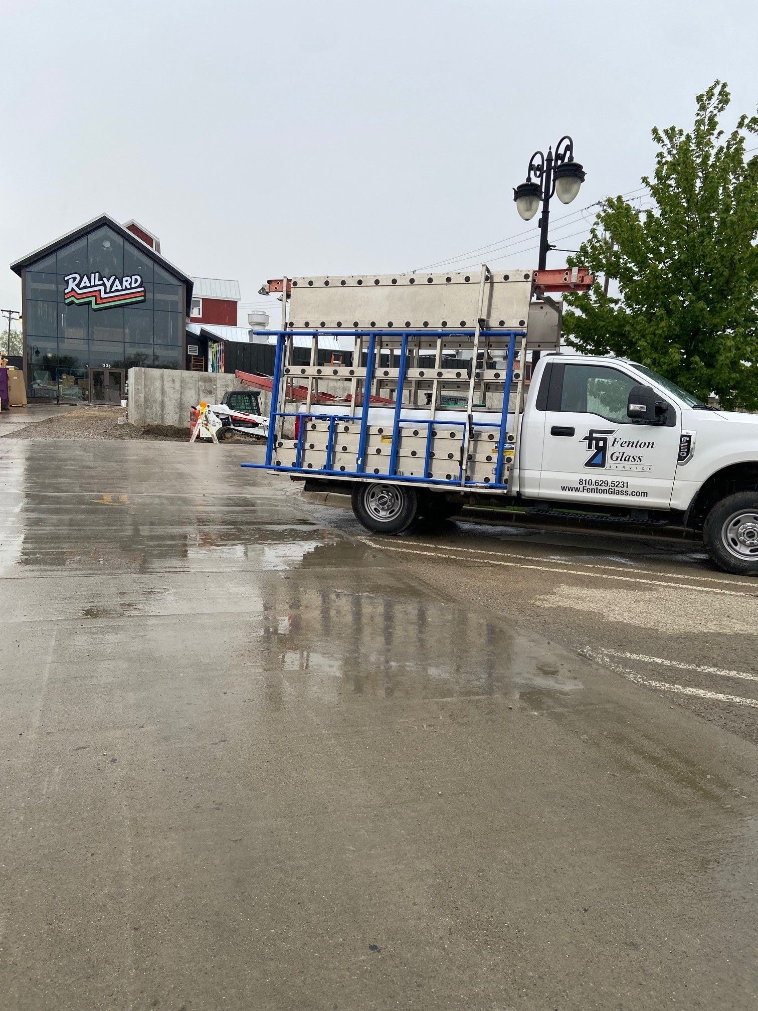 White truck carrying glass panes on a wet pavement near a building with a sign on a cloudy day.