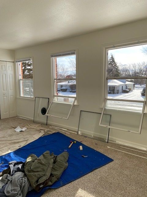 Room with three windows, snow outside. Window frames and a tarp on the floor.