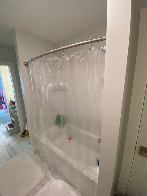 A clear shower curtain encloses a white bathtub in a bathroom.