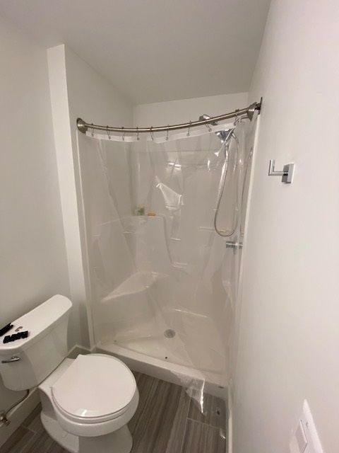 Small bathroom with a shower, toilet, and white walls. Transparent shower curtain is closed.