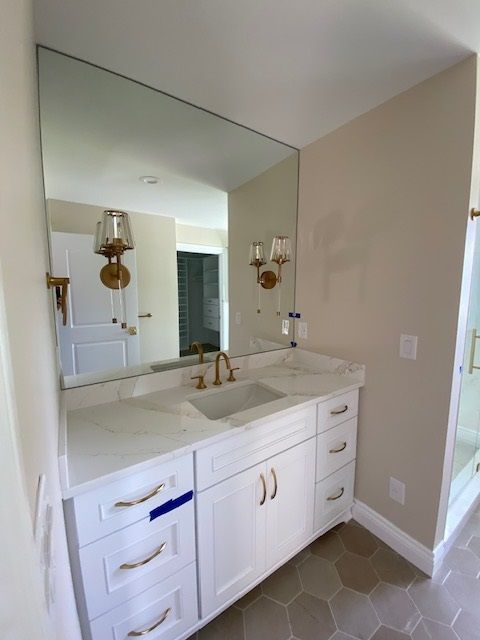 White bathroom vanity with marble countertop, gold fixtures, and large mirror.