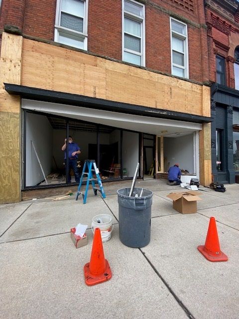Storefront under renovation; two workers inside, tools and cones on sidewalk.