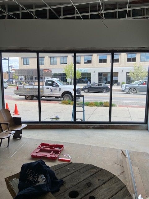 Interior view of a building with large windows overlooking a street with vehicles. Construction materials are visible inside.