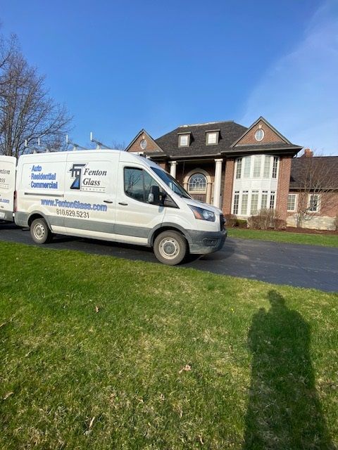 White van parked on lawn in front of a large brick house.