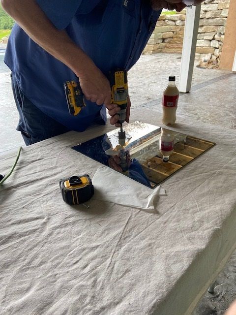 A person drilling a hole in a mirror on a table covered with a white cloth.