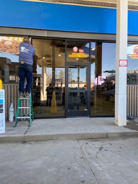 A person on a ladder cleans a glass door at a convenience store.