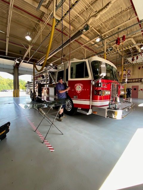 Man stands by red and white fire truck in a fire station bay.