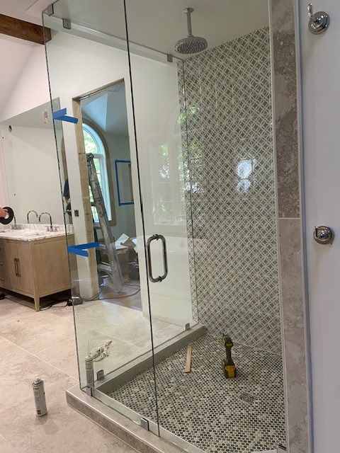 Bathroom with clear glass shower, pebble floor, patterned tile wall, and light wood vanity.