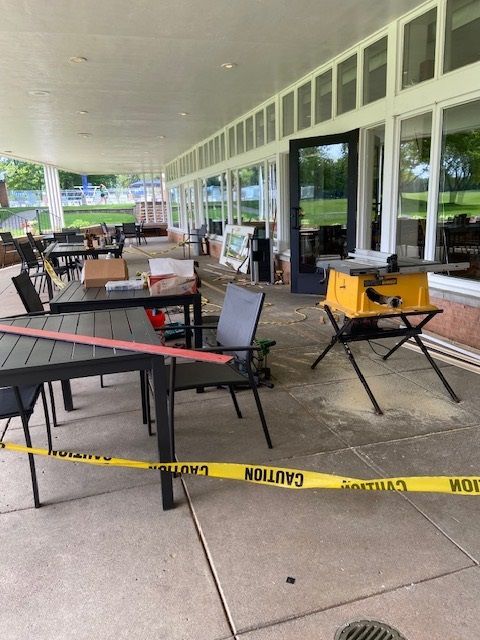Construction site. A yellow table saw on legs, caution tape, tables, and debris on a patio.