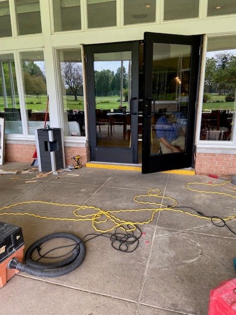 Exterior view of a building entrance with open black doors and construction materials on the patio.