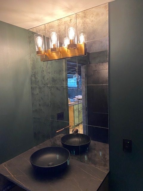 Vanity area with a large mirror, two black sinks, and a gold light fixture. Green walls and a dark countertop.