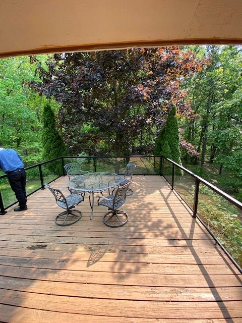 Wooden deck with table and chairs surrounded by trees; person on the left.