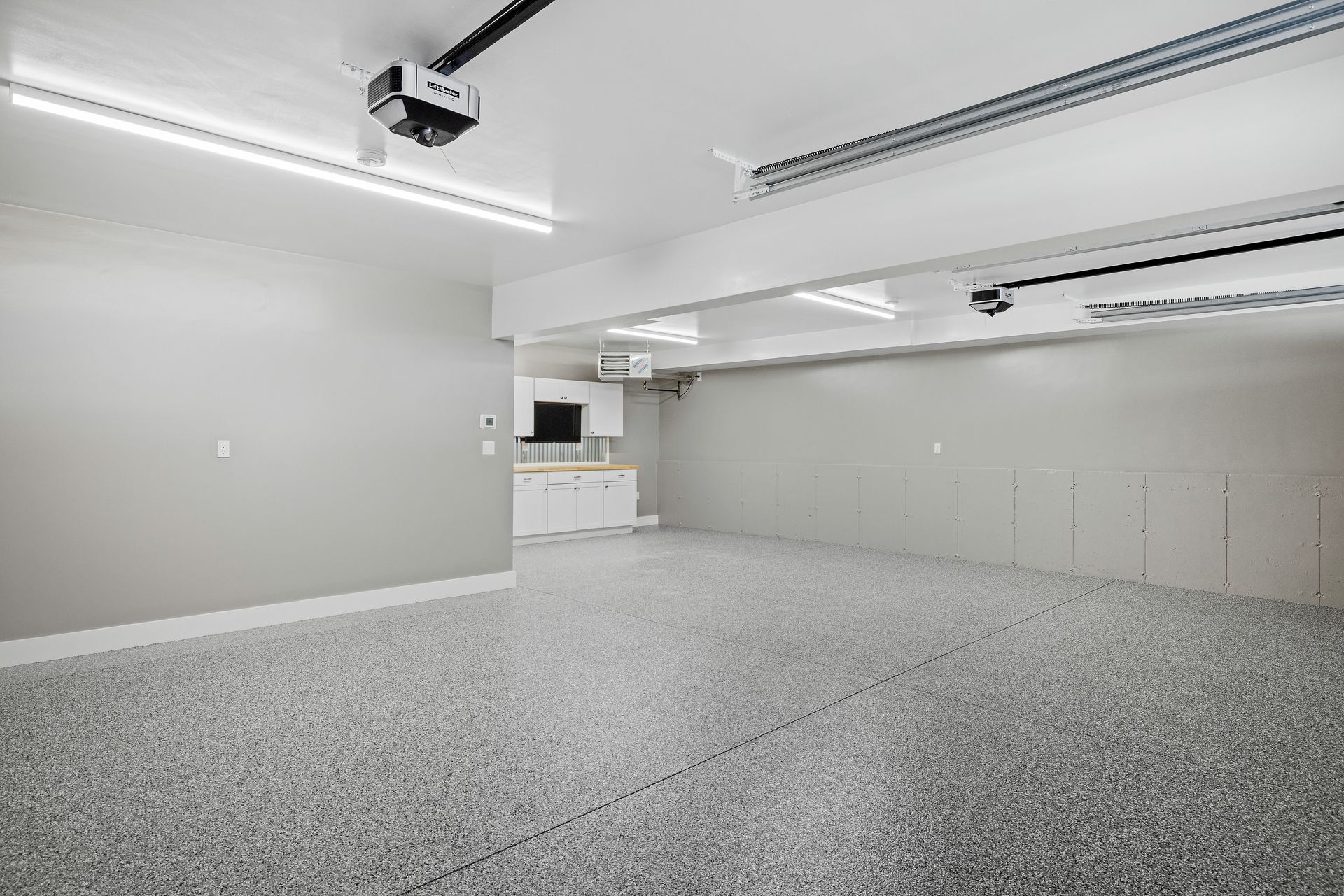 An empty garage with a garage door open and a kitchen in the background.