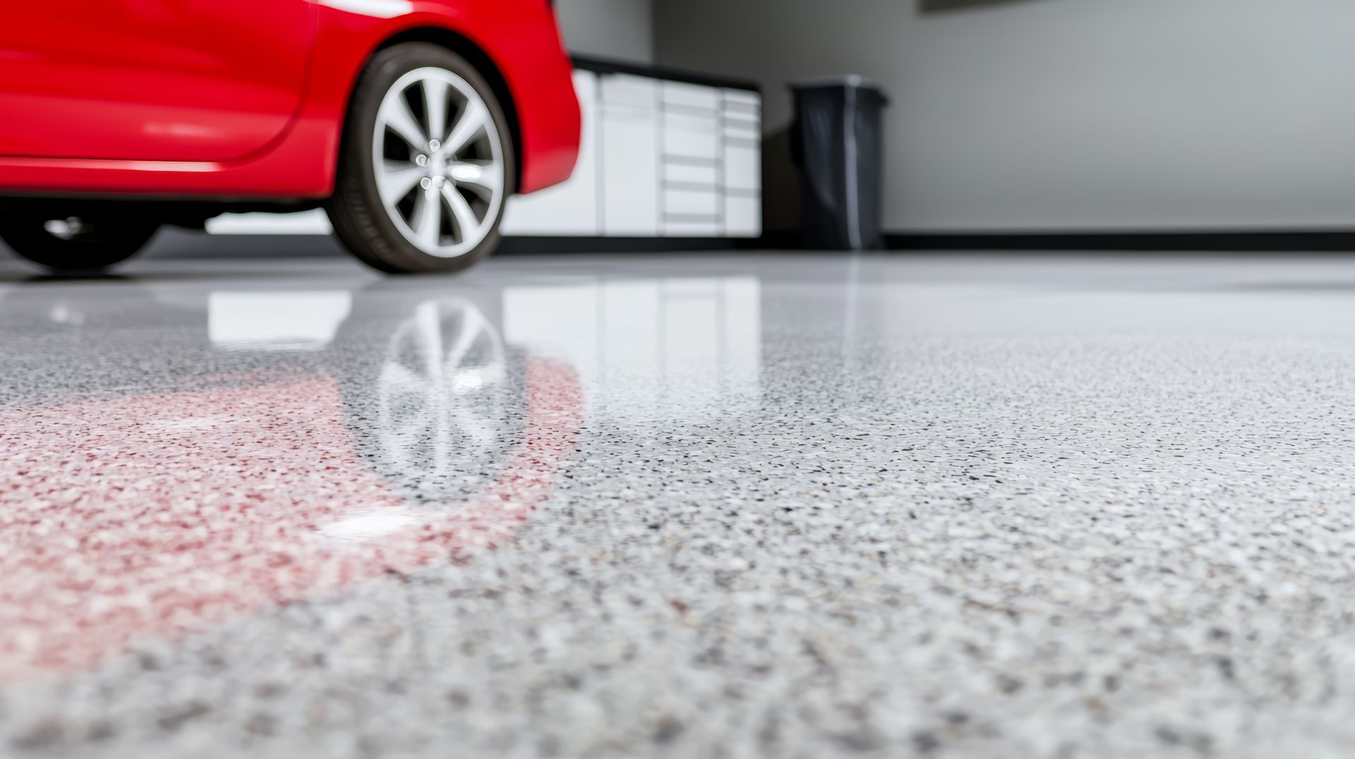 Red car parked on a shiny, speckled gray garage floor; reflections of the car visible.