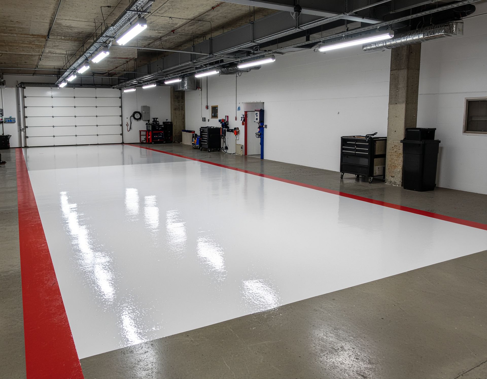 Large garage with shiny white floor, red border, overhead lights, and garage door.