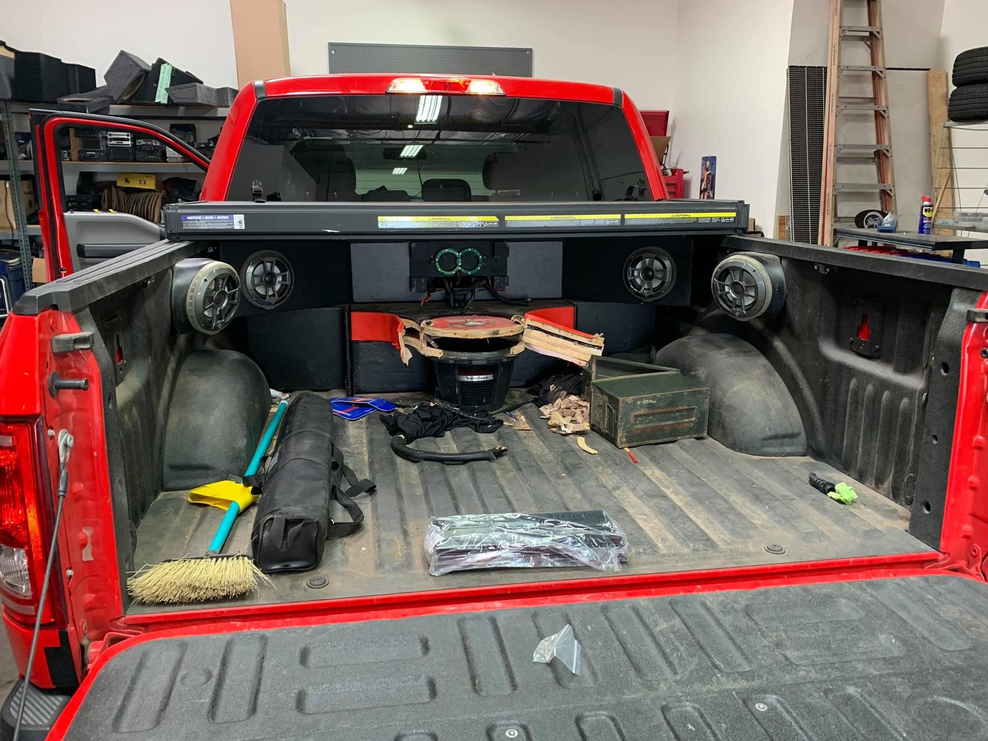 Red pickup truck bed with custom audio setup including speakers, subwoofers, and components.
