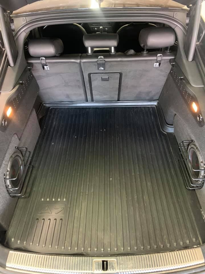 A car trunk with a rubber floor mat, subwoofer speakers, and back seats folded down. Black and gray interior.