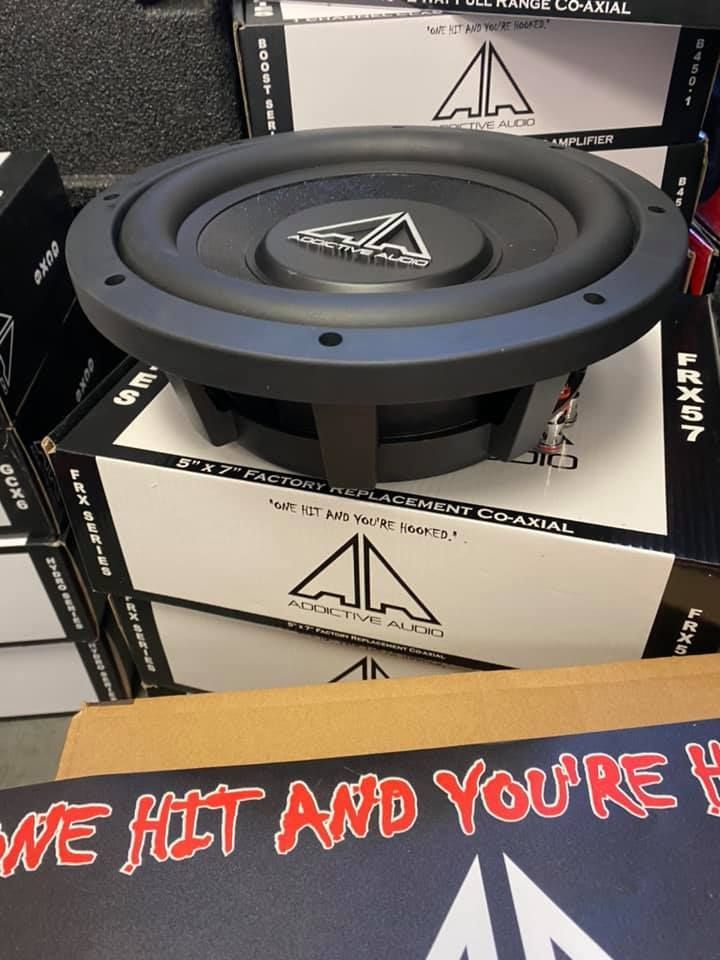 A black subwoofer sits on top of boxes of audio equipment, with the company logo visible. 