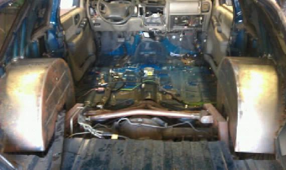 Interior of a teal vehicle stripped of seats and flooring, revealing the chassis and wheel wells.