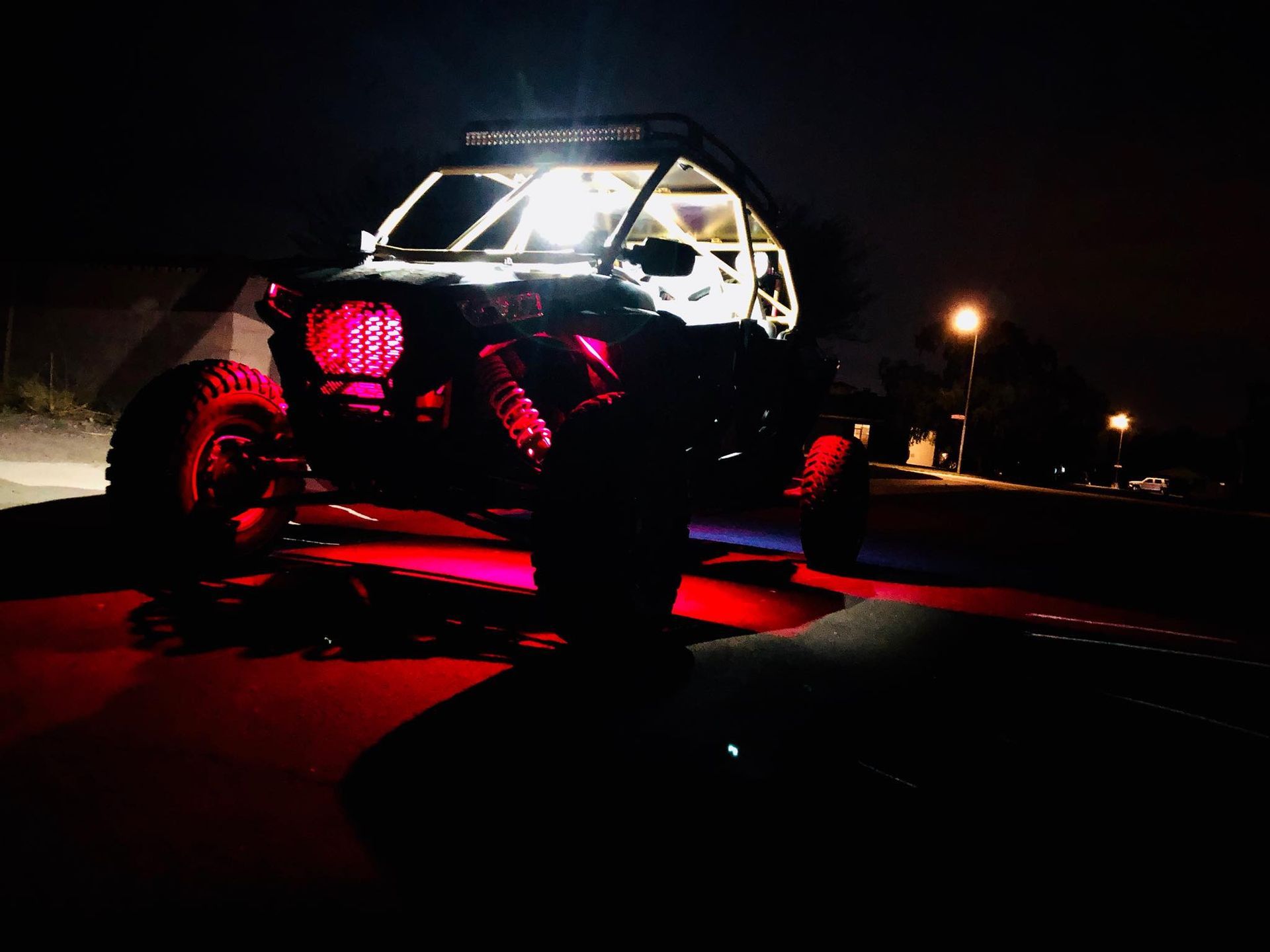 Off-road vehicle lit up with red and white lights at night. The vehicle has a roll cage.