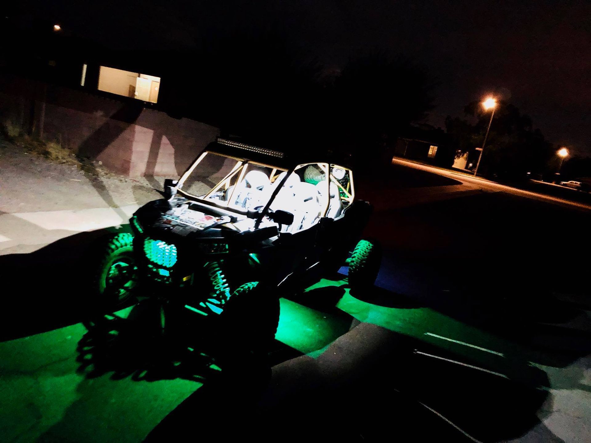 Dark ATV with green underglow lights, lit at night. Two people visible inside the vehicle, parked on a street.