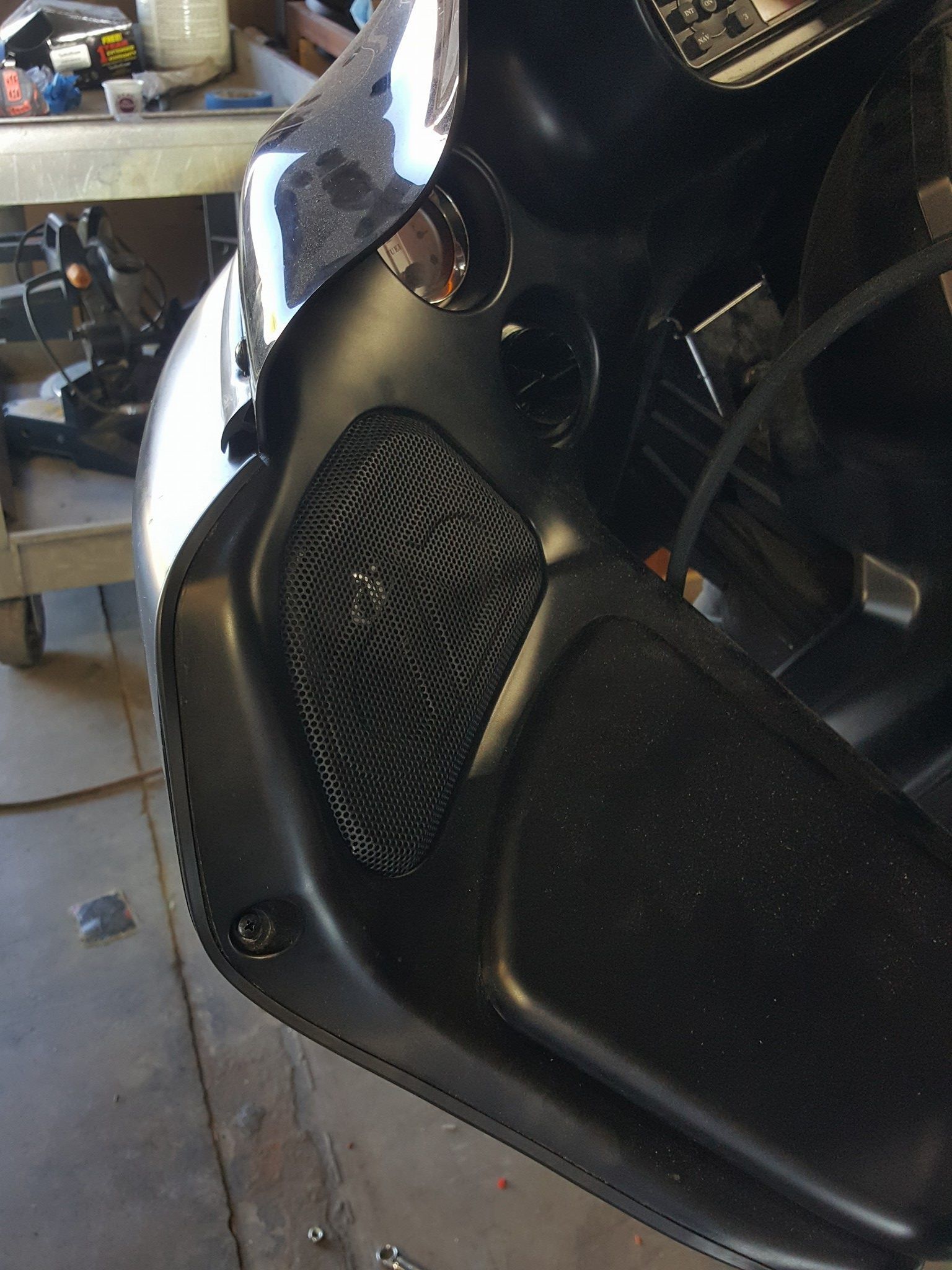Black motorcycle fairing with speaker grill, likely part of the dashboard or side panel.