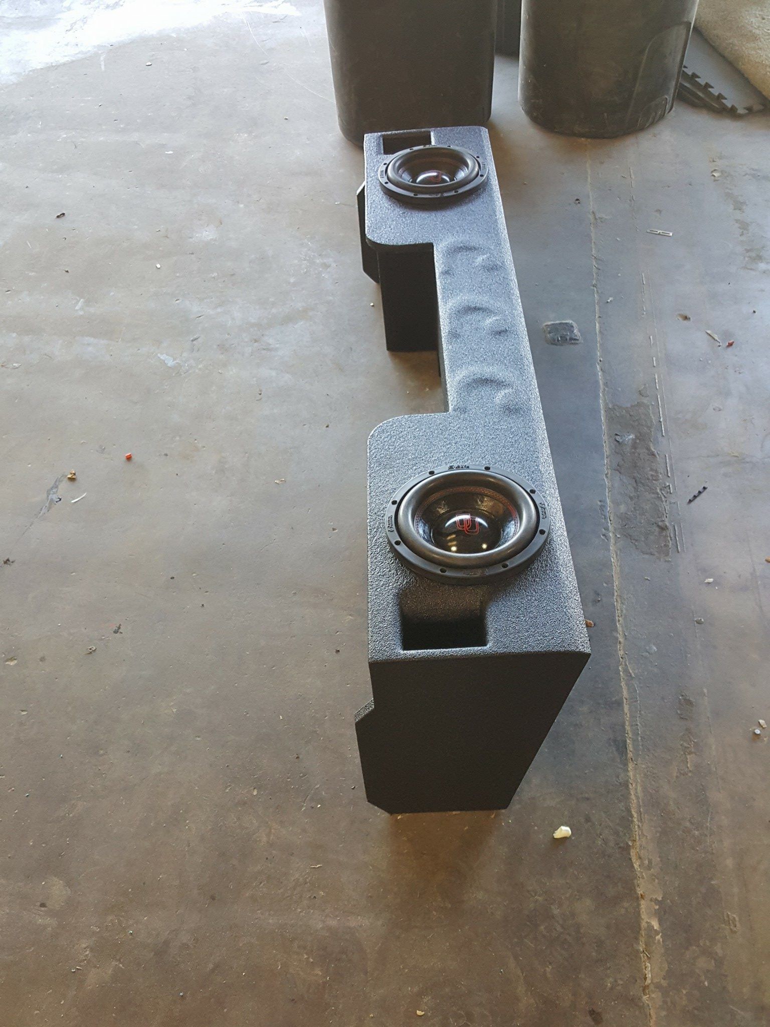Black speaker box with two speakers, on a concrete floor.