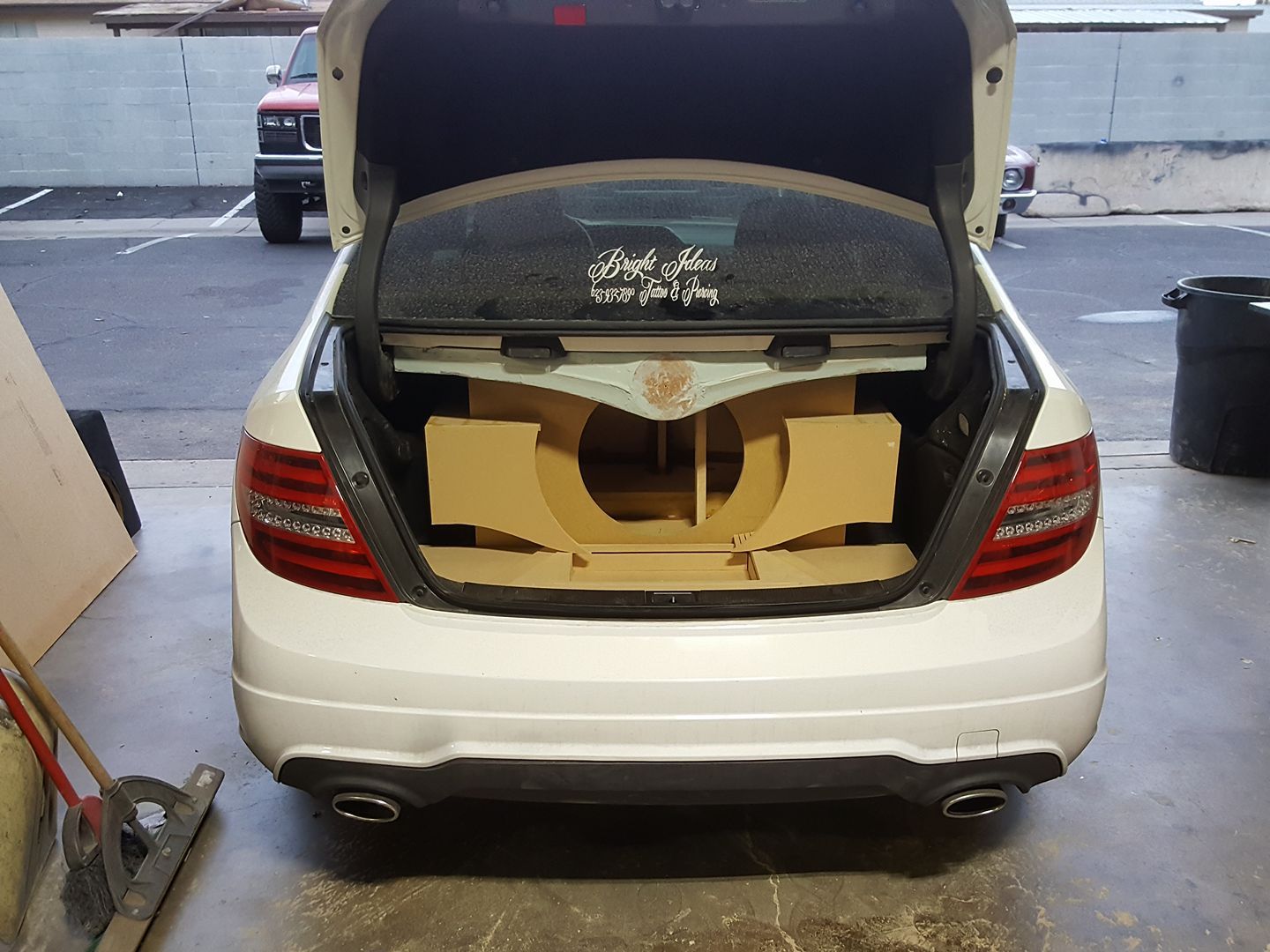 A white Mercedes-Benz with its trunk open, showcasing a custom wooden subwoofer enclosure.