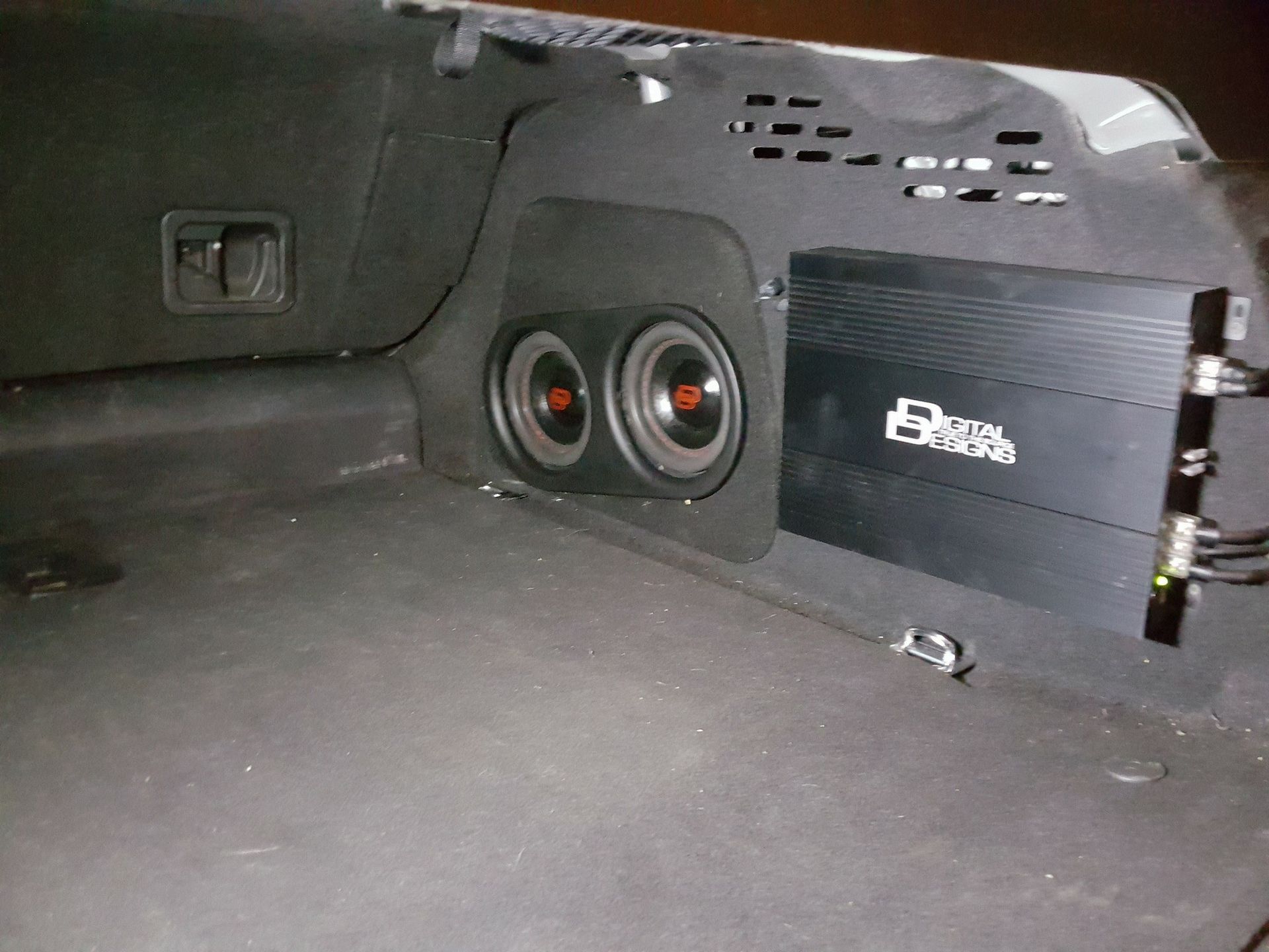 Black car trunk with two subwoofers and an amplifier mounted on a custom panel.
