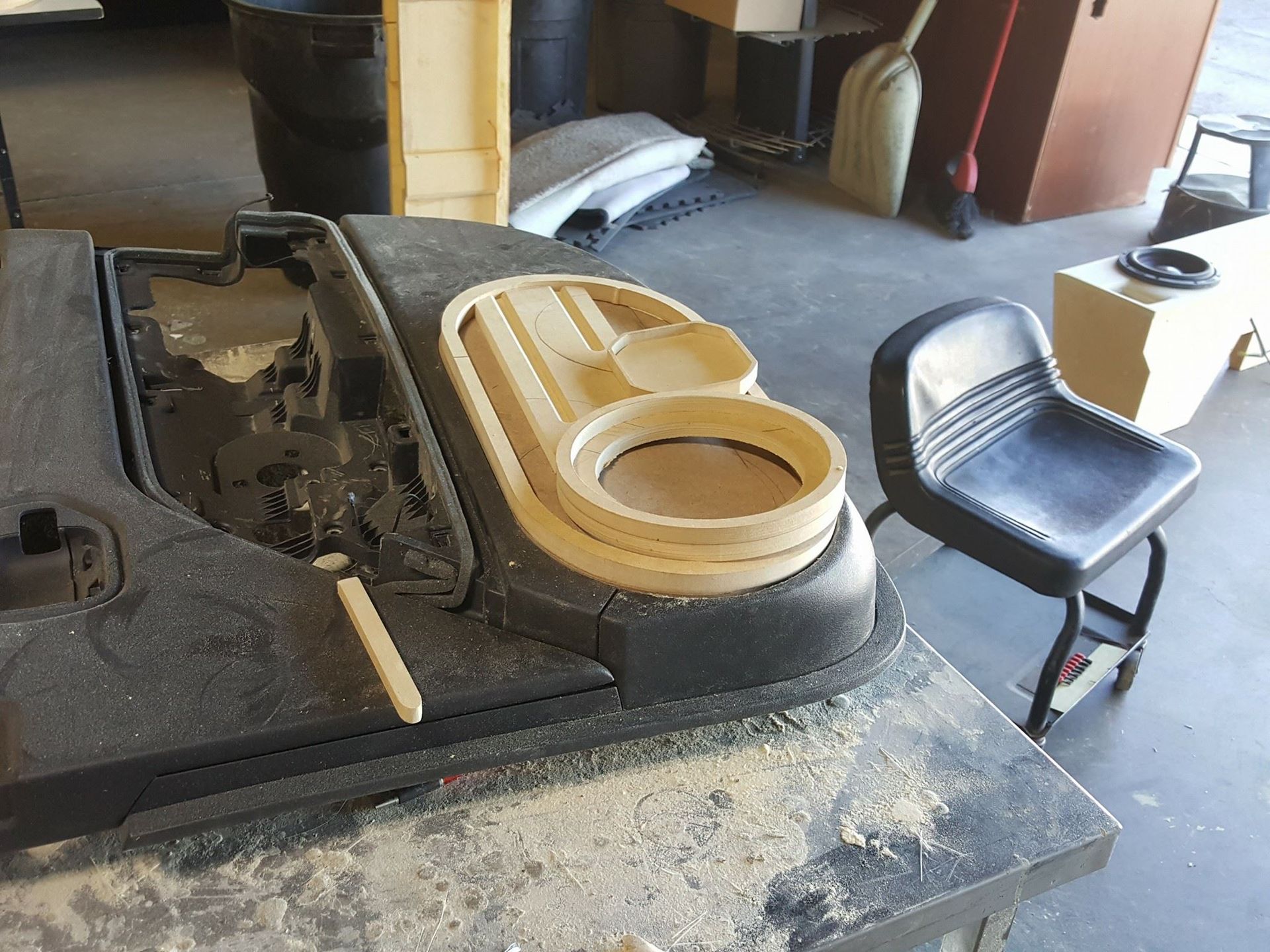 A partially disassembled black golf cart dashboard with a custom wooden speaker enclosure and a black stool in a workshop.
