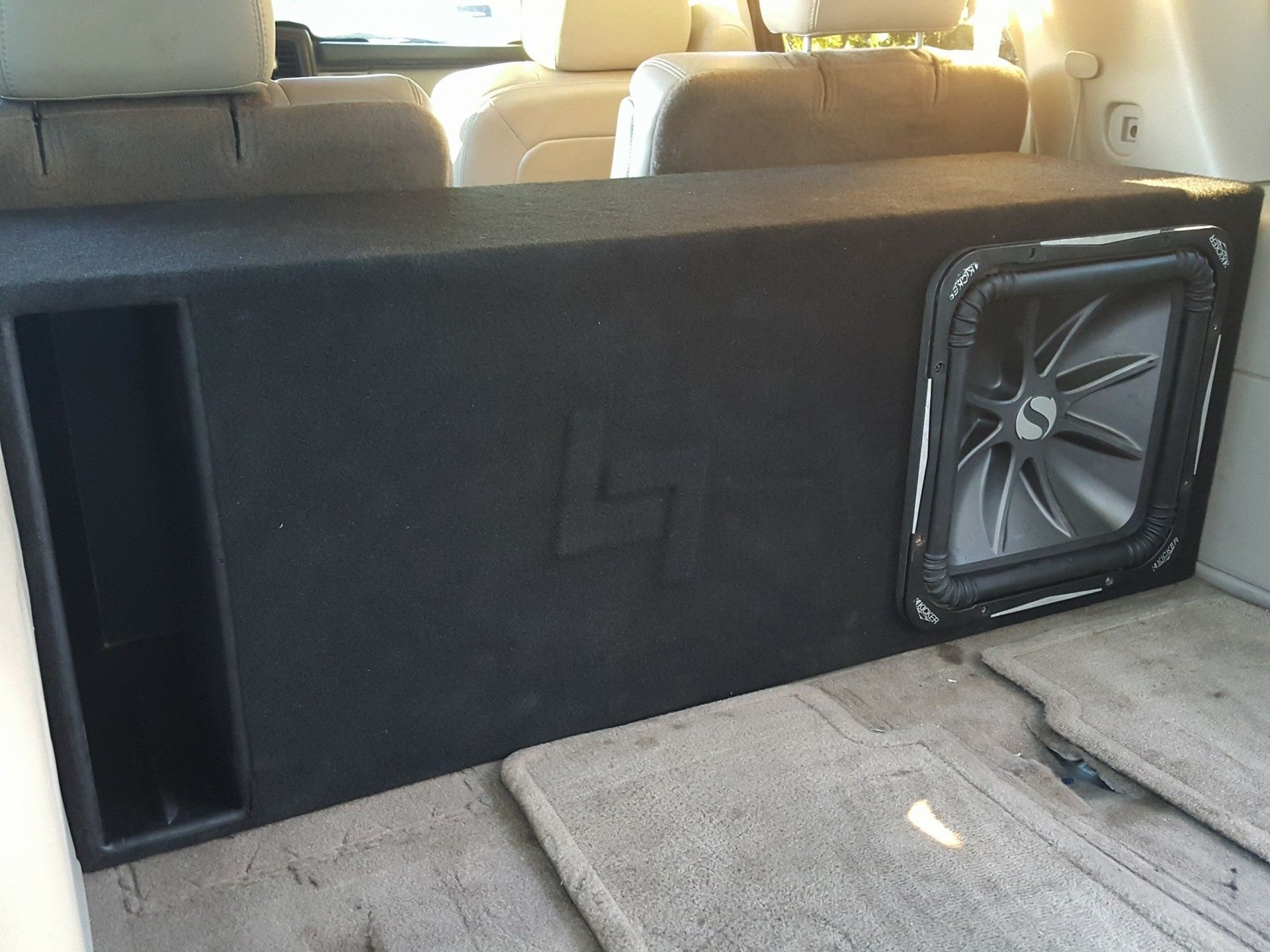 A black subwoofer box with a speaker in the trunk of a light-colored SUV.