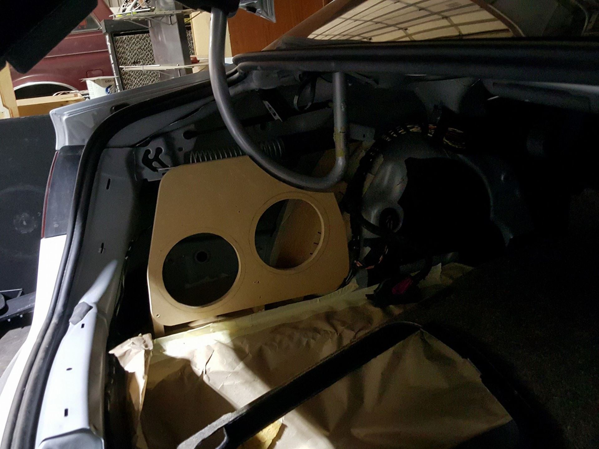 Inside of a car trunk; a tan speaker box with two circular cutouts sits against the back wall.