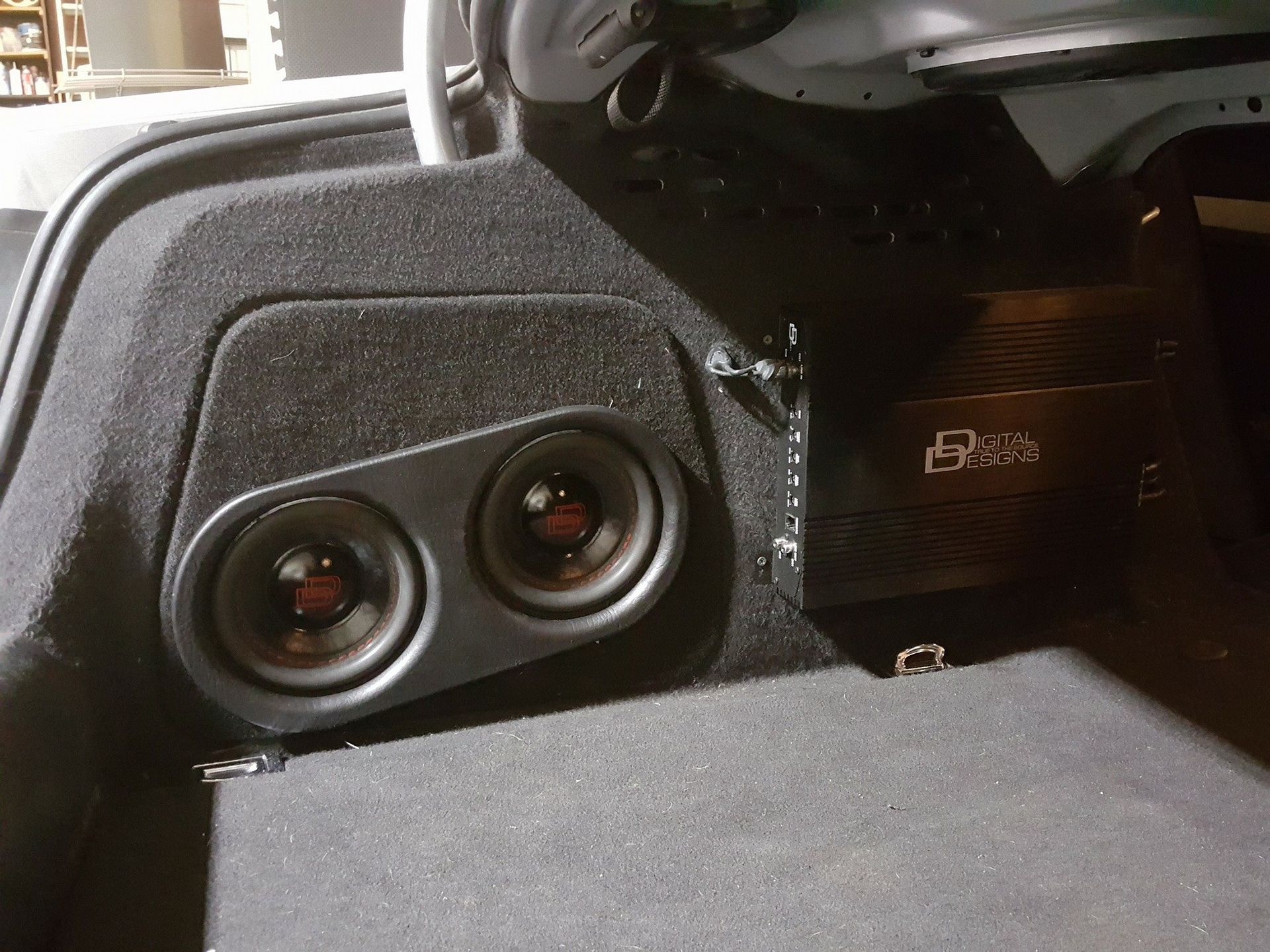 Two speakers and an amplifier installed in the trunk of a car, covered in black fabric.