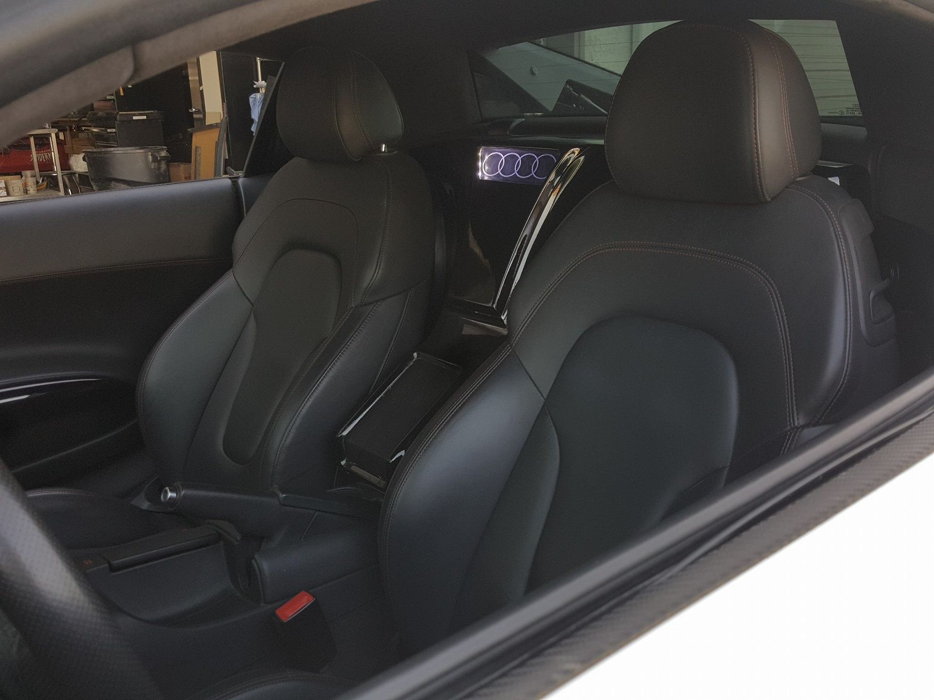 Black leather interior of a white Audi sports car, showing the seats, console, and a view through the side window.