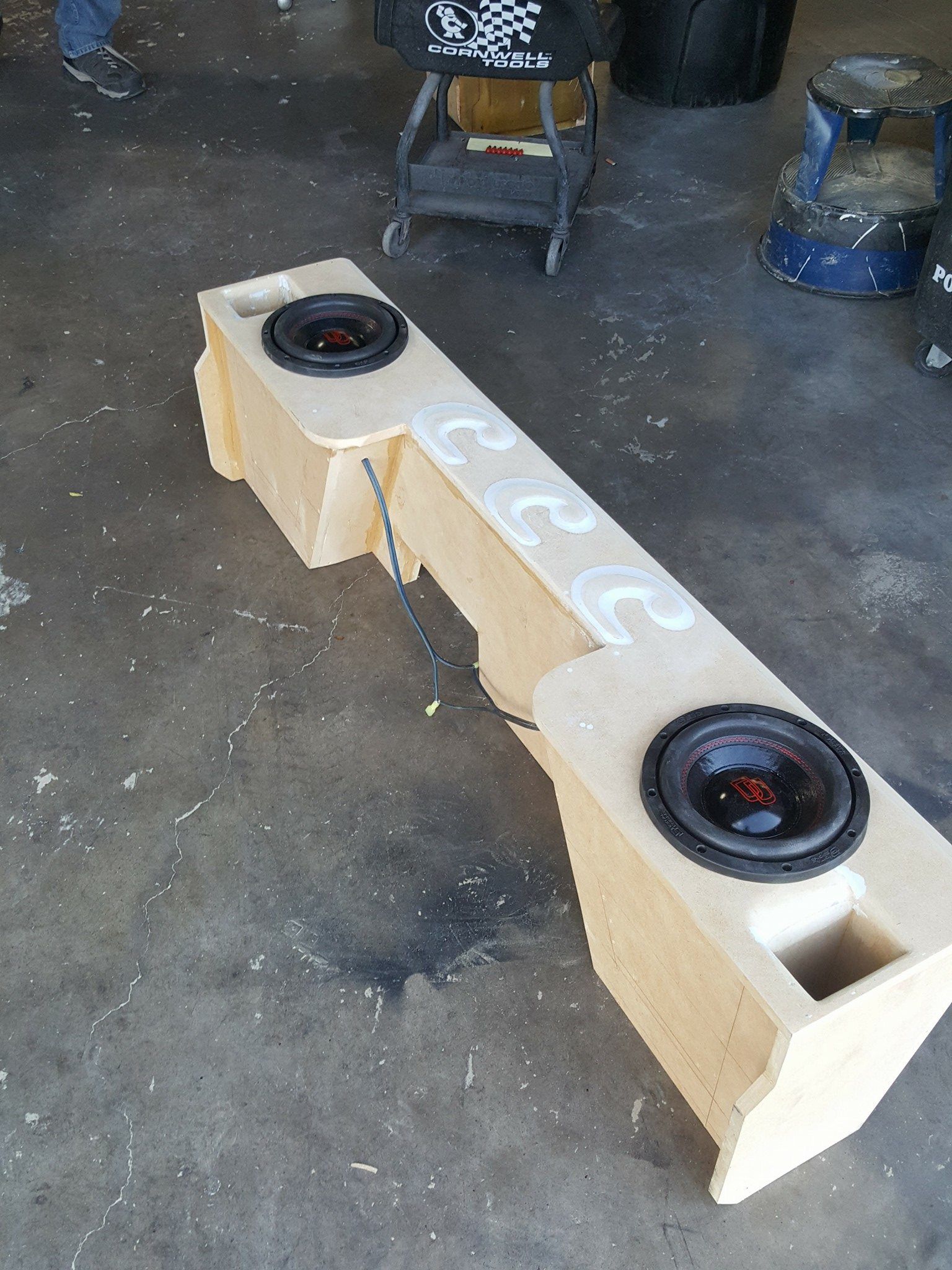 A wooden speaker box with two speakers installed, sitting on a concrete floor.