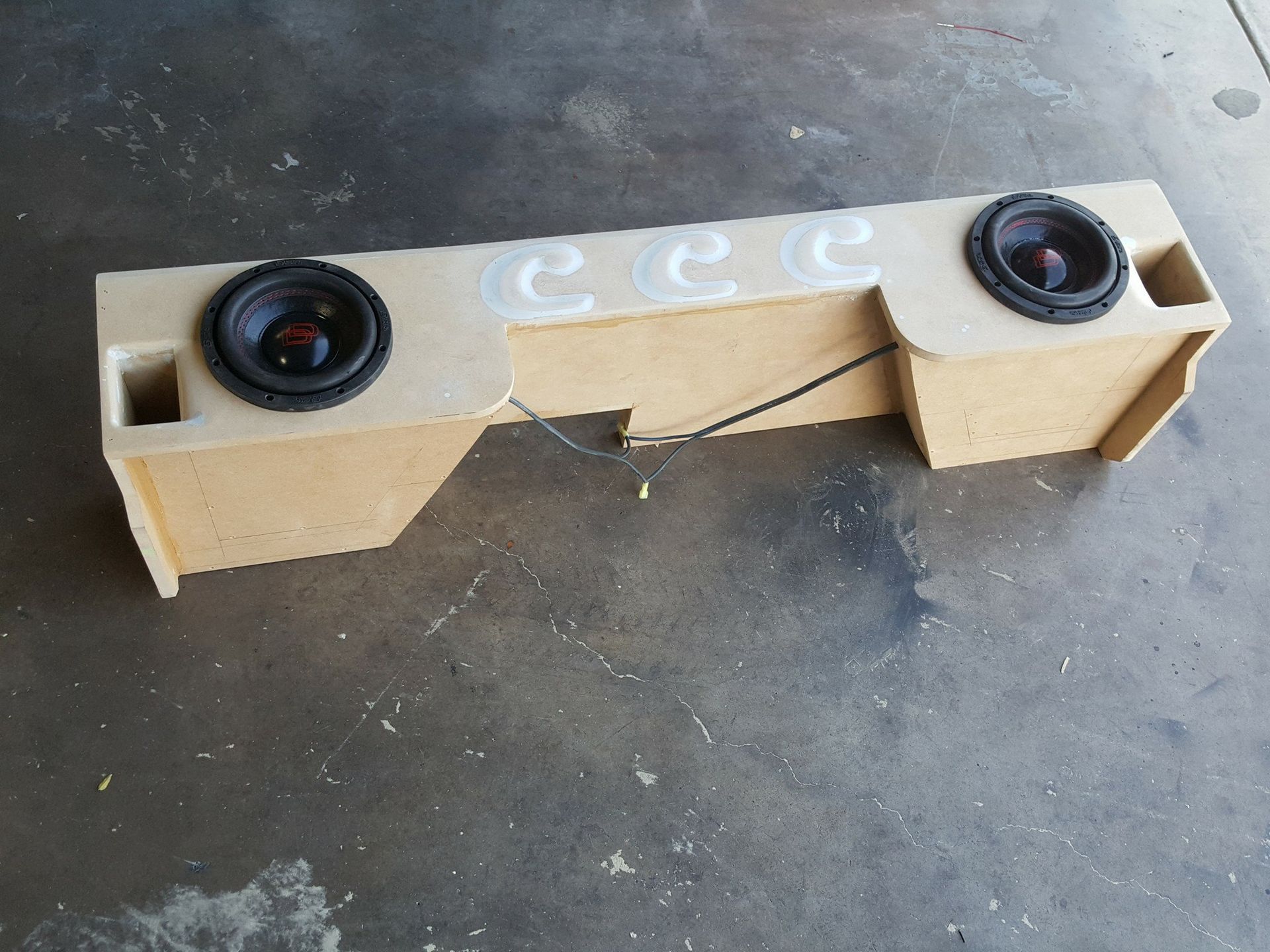 A custom-built tan speaker box with two black speakers, designed for a vehicle.  