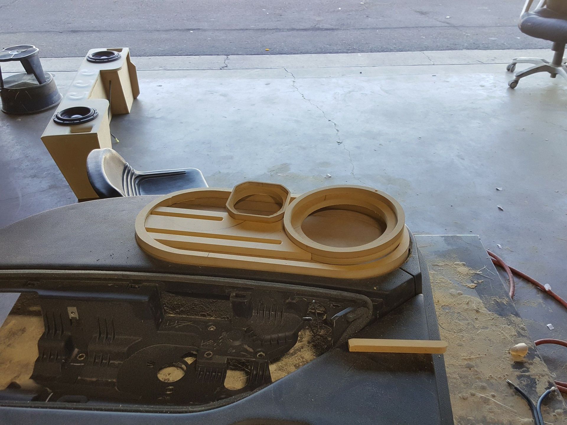 Wooden car audio components on a workbench in a garage, with speaker rings, boxes, and cutting debris.