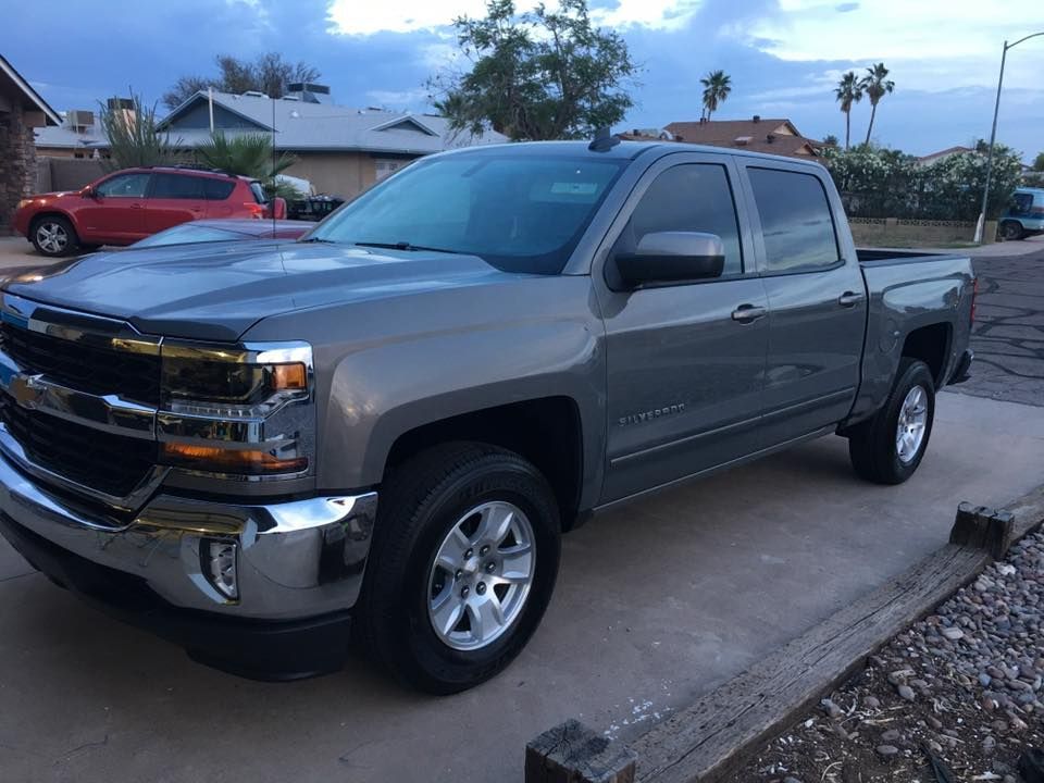 Gray Chevrolet Silverado pickup truck parked on a concrete driveway in front of a house.