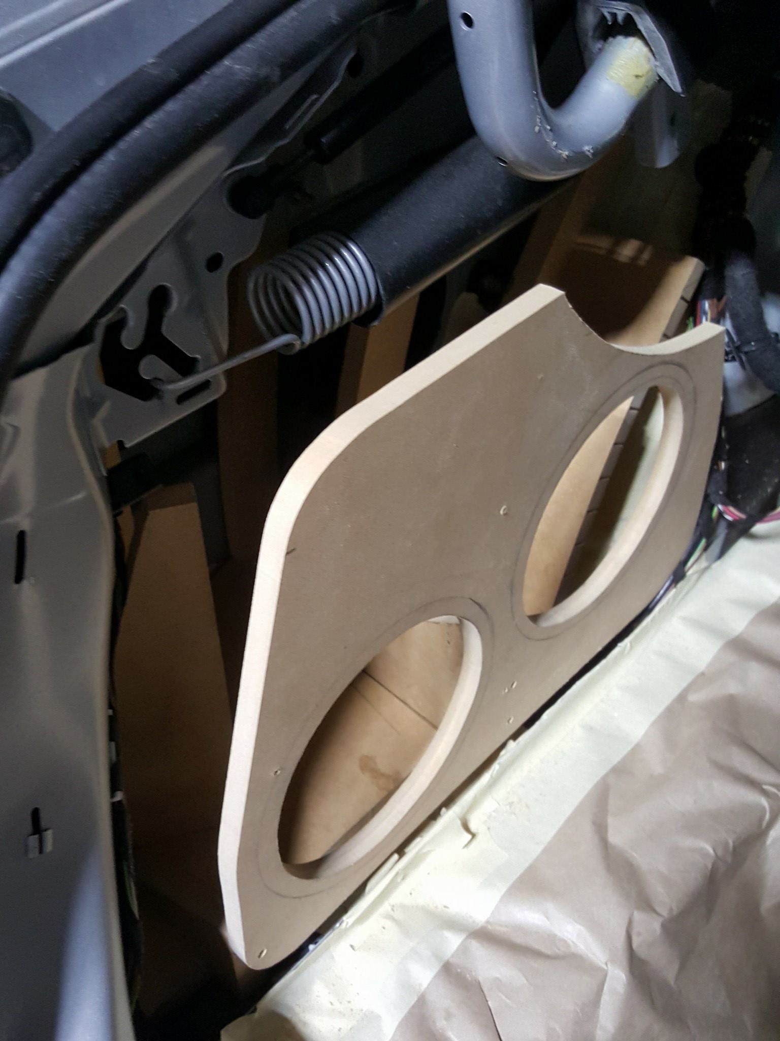 A custom subwoofer enclosure made of light brown wood, mounted in a vehicle's trunk area, featuring two speaker openings.