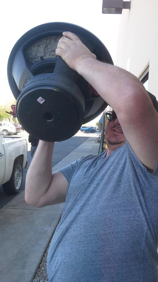 Man holding a large black subwoofer, likely for car audio.