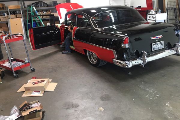 A classic black and red car in a garage, with the door open and a person working on it.