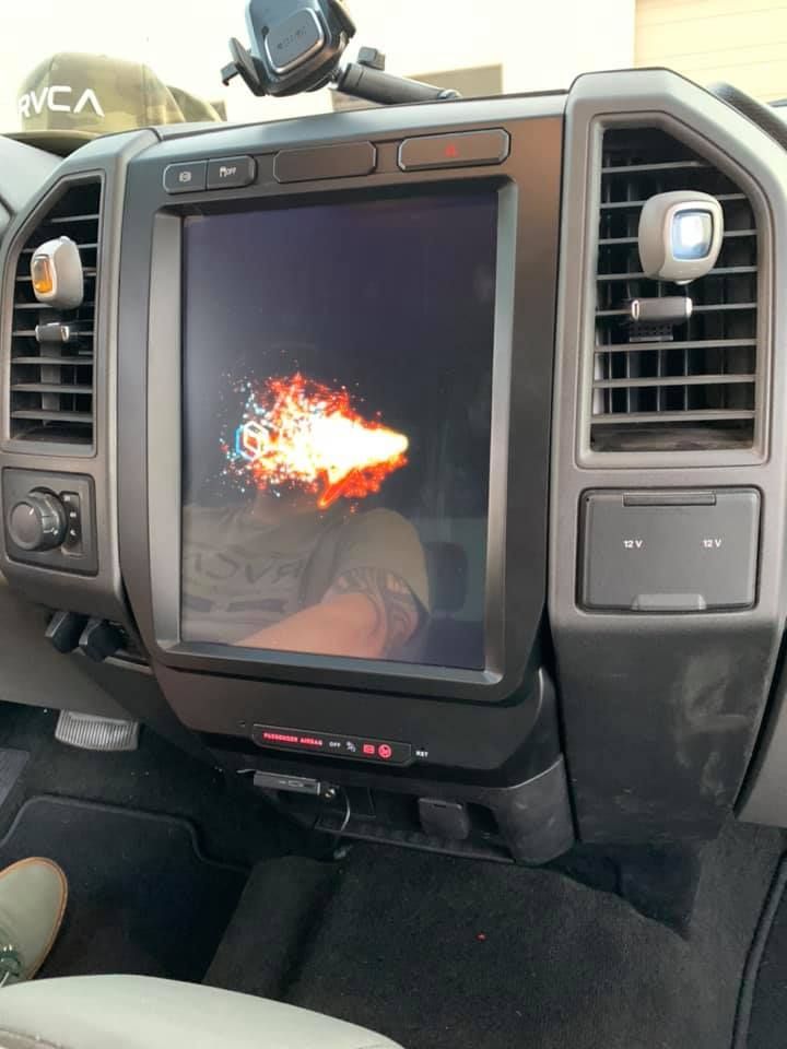 Large touchscreen car infotainment system displaying a fiery animation, mounted in a black dashboard.