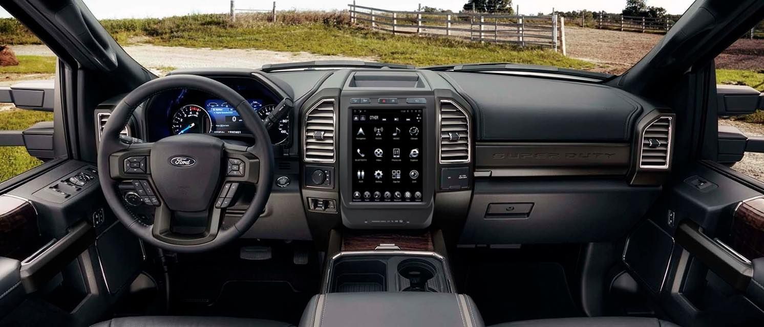 Interior view of a Ford truck dashboard. Features a large touchscreen display, steering wheel, and wood-grain accents.