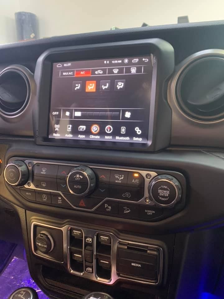 Interior view of a Jeep dashboard with a large touchscreen display and climate control knobs and buttons.