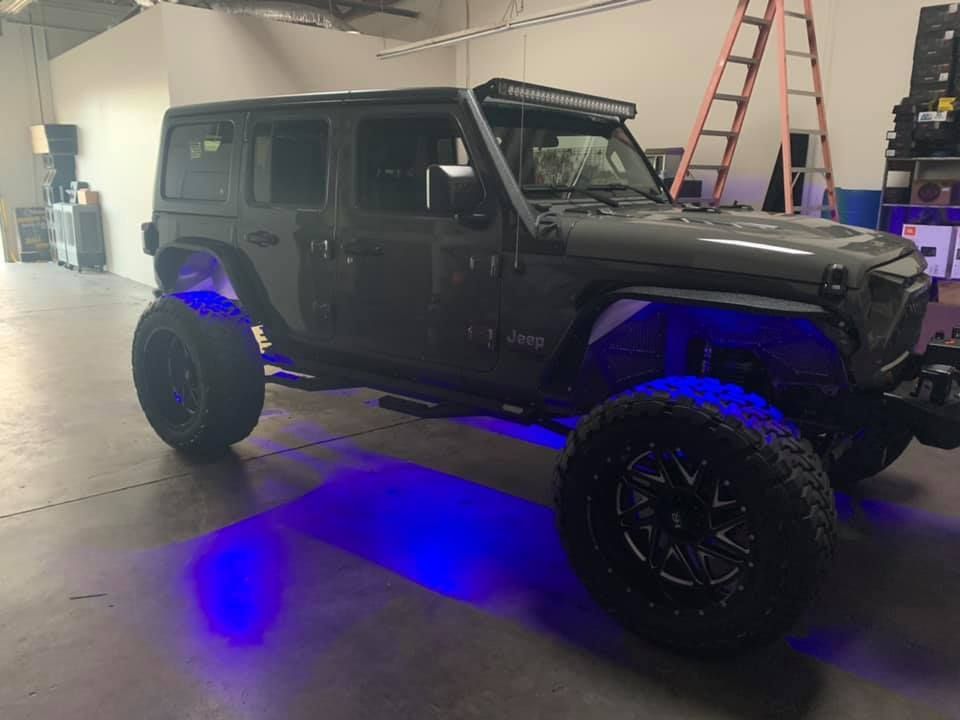 Dark gray Jeep with large black wheels, illuminated by blue underglow in a garage.