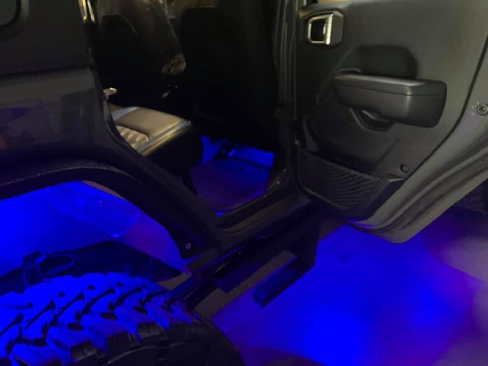 Interior of a Jeep with blue underglow lighting. The door is open, revealing the seats and interior.