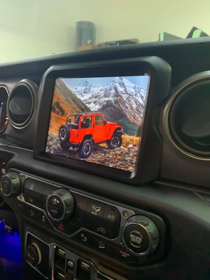 Dashboard of a car featuring a large screen displaying a red Jeep in a mountainous setting.