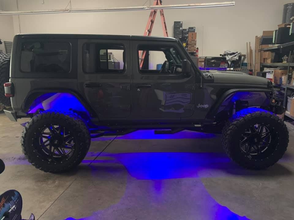 Dark gray Jeep with blue underglow, large black wheels, inside a garage.