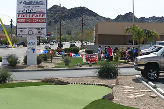 A commercial building with a mini-golf course in front; a group of people stand nearby.
